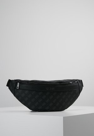 Banane Guess noire texturée avec poche zippée à l'avant et sangle ajustable, présentée sur un socle blanc sur fond gris.