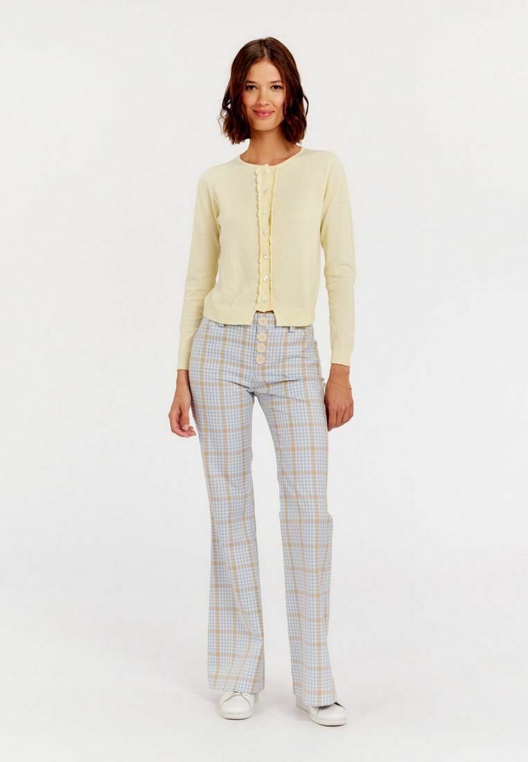 Cardigan jaune clair avec un bord à volants et des boutons, associé à un pantalon évasé à carreaux bleus avec de grands boutons à l'avant et une texture lisse.