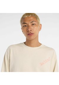 Cremfarbener Pullover mit rundem Ausschnitt. Verfügt über ein rosa gesticktes Logo auf der linken Seite. Das Material scheint weich mit einer glatten Textur zu sein.