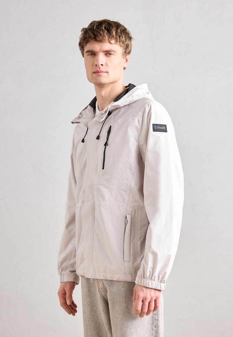 Light grey, lightweight jacket with a hood, black zipper details, elastic cuffs, and a visible logo on the left shoulder.