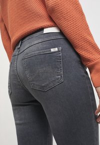 Vaqueros de mezclilla gris con un diseño ajustado, bolsillos traseros de forma puntiaguda distintiva y una textura sutil. Etiqueta blanca en la cintura.