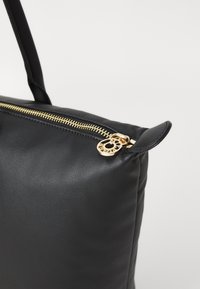 Sac à main en cuir noir avec une texture lisse, fermeture à glissière dorée et quincaillerie décorative. Présente une fermeture en haut et une poignée robuste.
