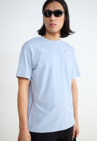 Light blue cotton T-shirt with short sleeves, featuring a white Puma logo and BMW Motorsport print, accented with a purple side stripe.
