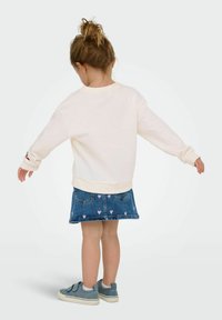 Sweatshirt crème à manches longues, associé à une jupe en denim sombre avec des motifs de cœurs roses. Chaussures bleues à enfiler confortables.