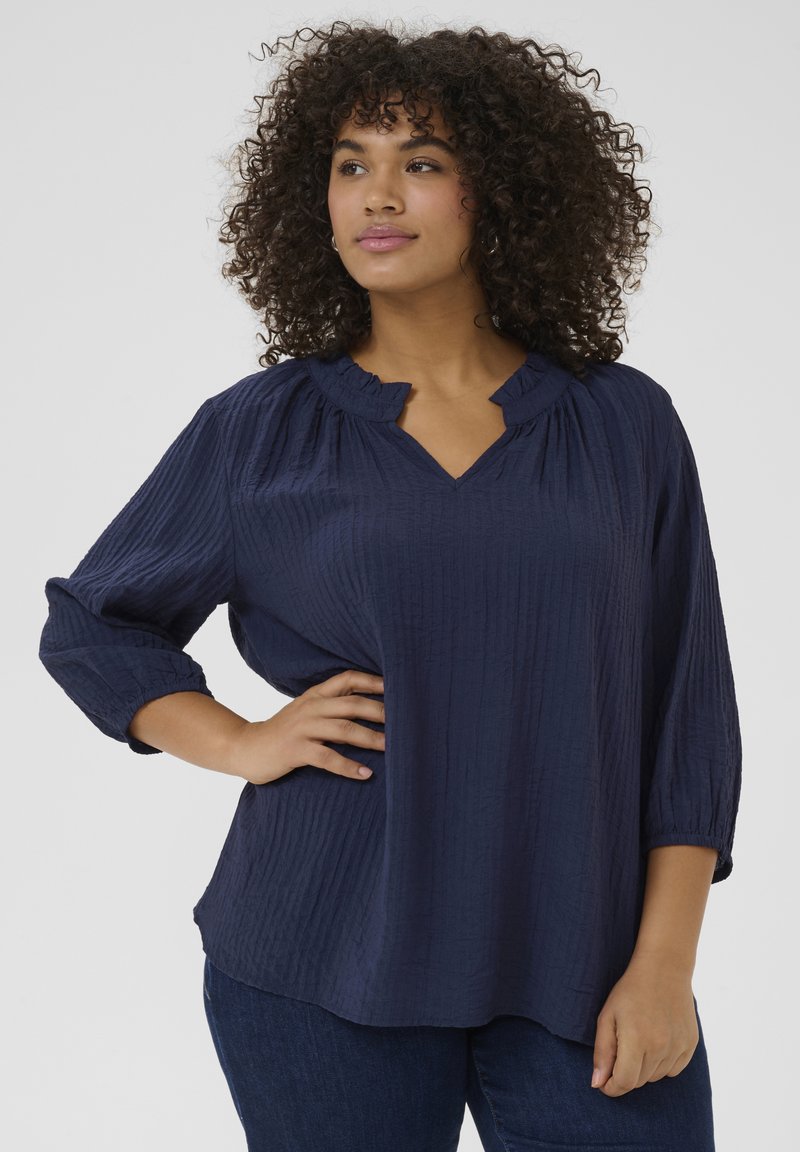 Marinebluse aus strukturiertem Stoff mit V-Ausschnitt und Rüschekragen. Mit Dreiviertelärmeln und lockerer Passform. Kombiniert mit Jeans im Denim-Look.