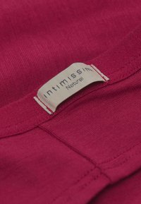 Bordeaux-stof met een zachte textuur en een klein, off-white label met de tekst "intimissimi" en "Natural" erop gestikt.