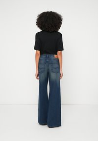 Jeans din denim albastru cu croială largă, cu spălare estompată, având talie înaltă, două buzunare în spate și o etichetă din piele cu brand pe talie.