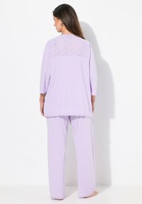 El conjunto de pijama lavanda presenta una blusa larga con un respaldo de encaje y bordes en forma de onda, acompañado de pantalones holgados. Textura de tela suave.