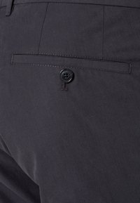 Tmavě šedá tkanina s texturovaným povrchem, obsahující zadní kapsu upevněnou černým knoflíkem. Jednoduchý a čistý design.