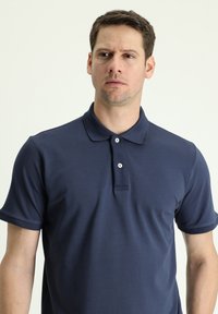Polo di colore blu navy realizzato in tessuto morbido, caratterizzato da colletto, patta con tre bottoni e maniche corte. Design minimalista senza motivi.