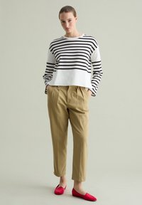Gestreiftes Langarmshirt in Schwarz und Weiß, beiges, plissiertes Hosenmodell und leuchtend rote Ballerinas. Schlichtes Design mit kontrastierenden Farben und Texturen.
