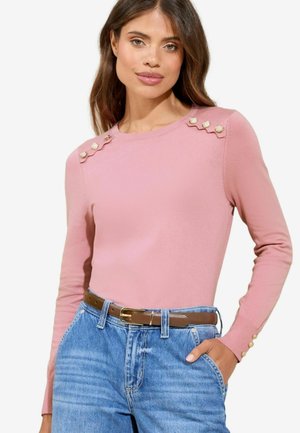 Roze lange mouwen trui met golvende schouderdetails en gouden accenten. Gepaard met hoge taille blauwe denim jeans en een bruine riem.