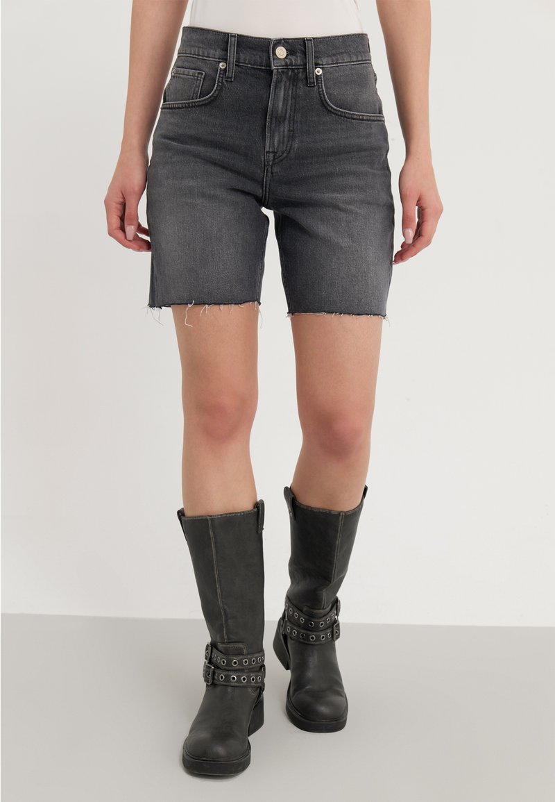 Shorts de mezclilla negra con dobladillo sin acabar, bolsillos frontales y una cintura alta, combinados con botas de cuero negras hasta la rodilla con detalles de hebilla.