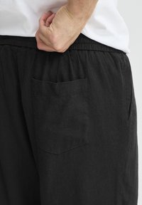 Sorte linnedbukser med elastisk talje og en enkelt baglomme. Stoffet har en mat finish og en let tekstur.