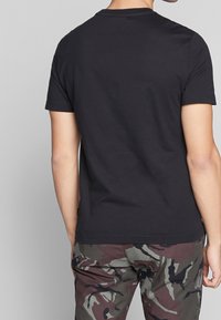 Camiseta negra de manga corta con cuello redondo, hecha de un tejido ligero; combinada con pantalones de camuflaje con tonos variados de verde y marrón.