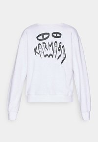 Sweatshirt blanc avec un design graphique noir au dos représentant des yeux et des mains stylisés, accompagné du mot "KARMA."