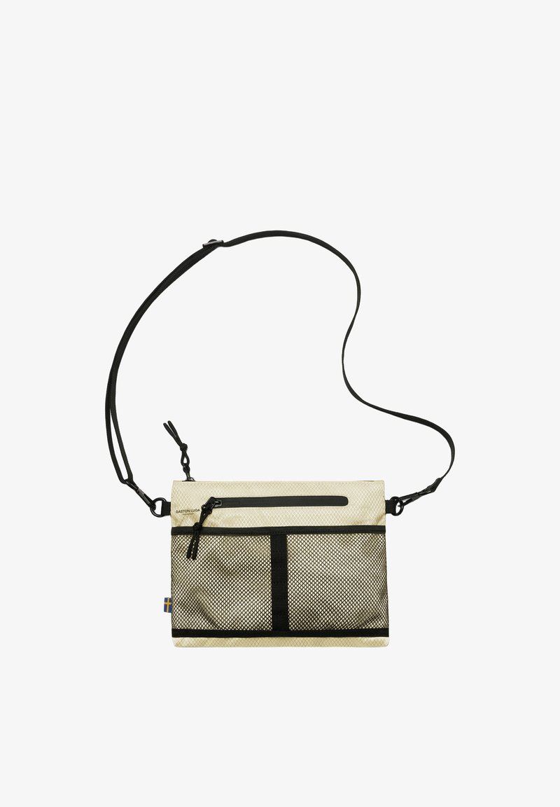 Sac bandoulière beige compact avec poche avant en maille noire, compartiments zippés, sangle noire réglable et petite étiquette avec drapeau suédois sur le côté.