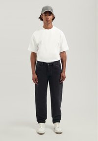 Biała koszulka z krótkim rękawem, czarne dżinsy, szara czapka i białe sneakersy. Prosty design, luźny krój, gładka tekstura, brak widocznych wzorów.