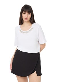 Biała koszula z krótkim rękawem z dekoltem w serek ozdobionym metalicznymi akcentami, w zestawieniu z czarną spódnicą typu wrap. Gładka struktura.