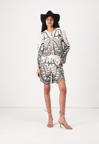 White embroidered top with black floral patterns, paired with matching shorts; model wears a wide-brimmed black hat and strappy nude heels.