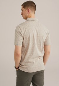 Camisa de manga corta en beige claro con un patrón geométrico. Presenta un cuello con solapa y un corte casual. Combinada con pantalones verde oliva.