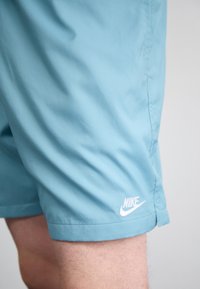 Calções Nike de azul claro, com uma textura suave, costura lateral e um logótipo da Nike branco na parte inferior da perna.