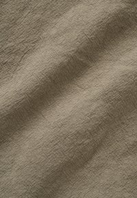 Beige linnenstof met zichtbare weving en natuurlijke kreukels, die textuur en zachte plooien toont onder diffuus licht.