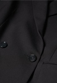 Schwarzer Blazer mit glatter Textur, zwei großen schwarzen Knöpfen und taillierten Nähten. Sauberes, minimalistisches Design ohne sichtbare Muster.