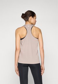 Débardeur de sport sans manches beige clair avec un design dos nageur, tissu texturé et accents noirs au niveau de l'encolure.