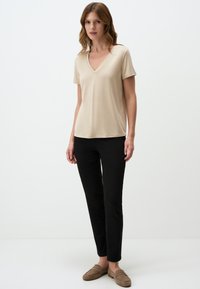 T-shirt beige con scollo a V e maniche corte, abbinato a pantaloni neri slim-fit e mocassini beige. Texture liscia, design informale.