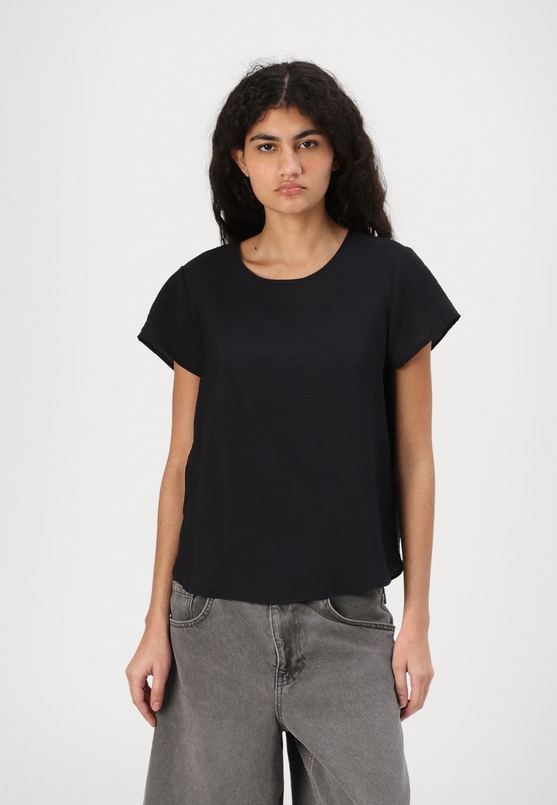 Top nero a maniche corte con scollatura rotonda, realizzato in un tessuto morbido. Abbinato a jeans grigi a gamba larga con una texture scolorita.