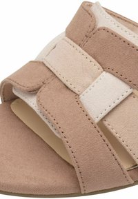 Sandales à glissière en tissu beige avec un design entrecroisé, une texture douce, un bout ouvert et une semelle plate. Détails de couture remarquables sur les lanières.
