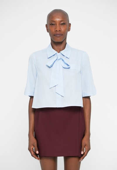 Chemise bleue coupée avec un nœud papillon au cou, manches courtes et texture linéaire subtile, assortie à une jupe bourgogne jusqu'aux genoux.