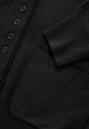Svart cardigan med ett mjukt, texturerat tyg, sex svarta knappar och en sidficka med ribbat detaljer på ärmarna.