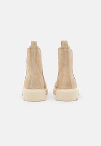 Bottines en daim beige avec une texture, dotées d'un bout rond et d'une semelle en caoutchouc épaisse. Coutures arrière accentuées.
