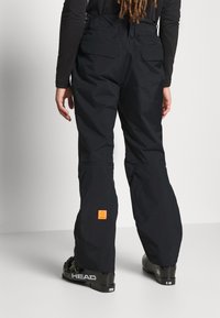 Sorte skibukser med en holdbar, glat tekstur, der har et orange mærkelogo. Designet med en afslappet pasform og forstærkninger ved anklerne.