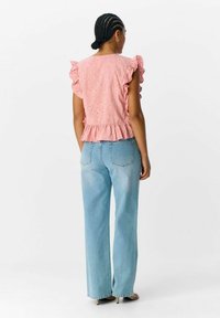 Różowa bluzka w stylu eyelet z falbanami na rękawach i peplum, w połączeniu z jasnoniebieskimi szerokimi spodniami. Gładka tekstura, kwiatowe wycięcia na tkaninie.