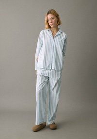 Conjunto de pijama a rayas azul claro y blanco, que incluye una camisa de botones con un bolsillo y pantalones holgados. Tejido suave y ajuste relajado.
