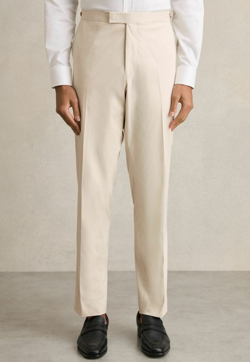 Pantalons beige ajustés avec un devant plat, des poches latérales et une coupe droite, associés à des mocassins noirs. Doux au toucher.