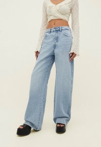 Jeans de pierna ancha de color azul claro con cintura alta, fabricados en denim. Presenta cinco bolsillos y un cierre de botón clásico. Top de encaje texturizado.