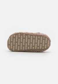 Chausson en fourrure rose clair avec une texture douce, semelle en caoutchouc présentant un motif répété du logo "crocs", bout arrondi et design rembourré.