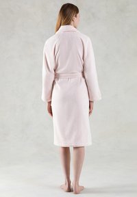 Accappatoio in terry cloth morbido, di colore rosa chiaro, con cintura, maniche lunghe e colletto sciallato. Tessuto liscio, lunghezza fino al ginocchio, senza motivi visibili.