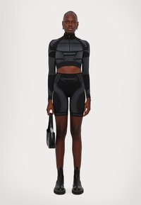 Mustmust mustrisikaga kõrge kraega ja pikkade varrukatega must sportlik crop top, millele on sobitatud kõrge vöökoht ja lühikesed püksid. Omab kontrastseid tekstuuriga mustreid.