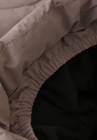Capucha acolchada con un exterior suave en taupe y ribete elástico, que revela un suave forro de forro polar negro en el interior.