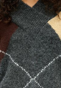Knitted sweater featuring a thick, textured fabric in dark gray, brown, and light beige with a diagonal pattern and contrasting white stitching.