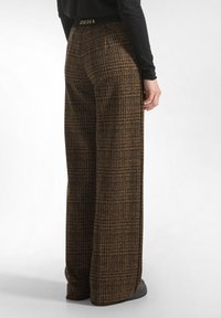Wide-leg pants in brown textured fabric featuring a checked pattern. Elastic waistband with "DEHA" logo and black shoes visible at the bottom.