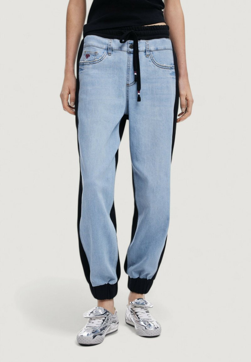 Pantalones jogger de color azul claro con paneles laterales negros, cintura elástica y cordón. Cuenta con bolsillos delanteros y puños de canalé.