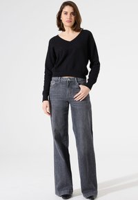 Pull noir à col en V texturé associé à un jean gris taille haute et à jambes larges. Le jean présente une fermeture à bouton et un design classique à cinq poches.