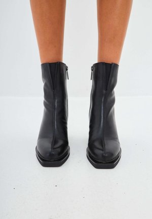 Botas de cuero negro hasta el tobillo con una textura suave, punta cuadrada y cremalleras laterales. Suelas planas con un diseño minimalista y elegante.