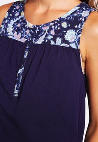 Blusa senza maniche blu navy con scollatura a yo-yo decorata, caratterizzata da leggeri motivi floreali e dettagli con bottoni al centro, con pieghe nella parte inferiore.